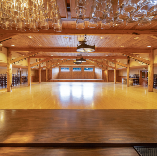 A large open ballroom room with a bar and hanging drink glasses in the foreground